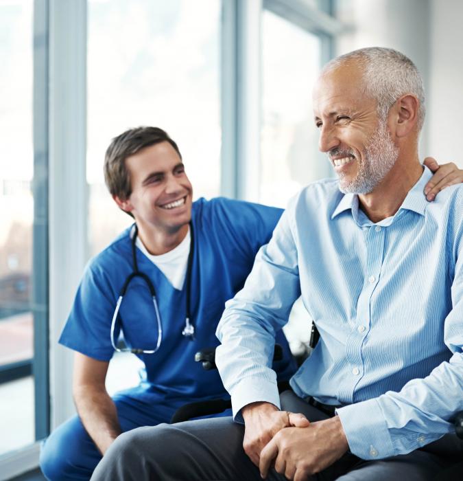 A male patient sitting in a wheelchair speaking with a provider. 